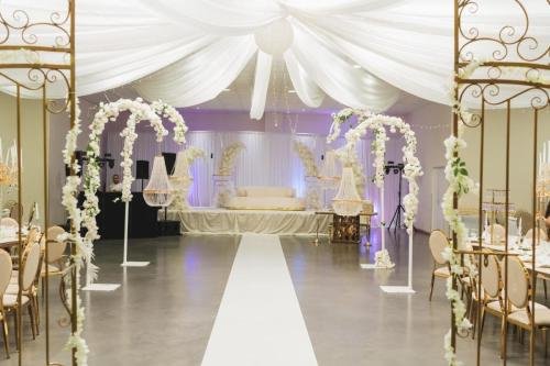 Grande salle de mariage blanche et or avec arches florales et estrade
